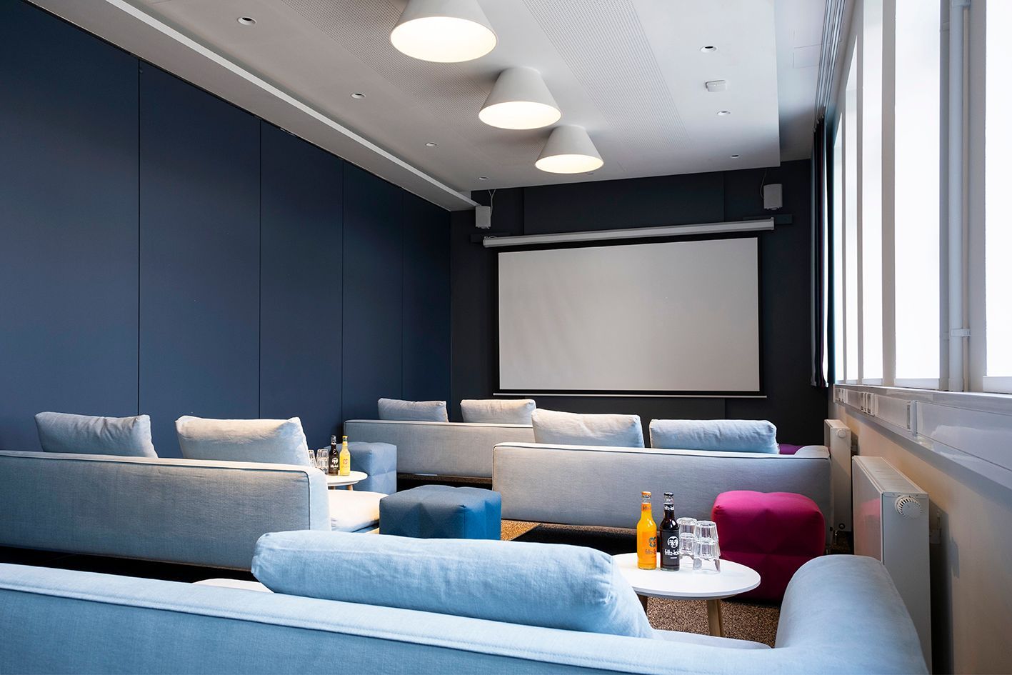Study III Meetingraum mit blauen Sofas, runden Tischen, Leinwand und großen Fenstern