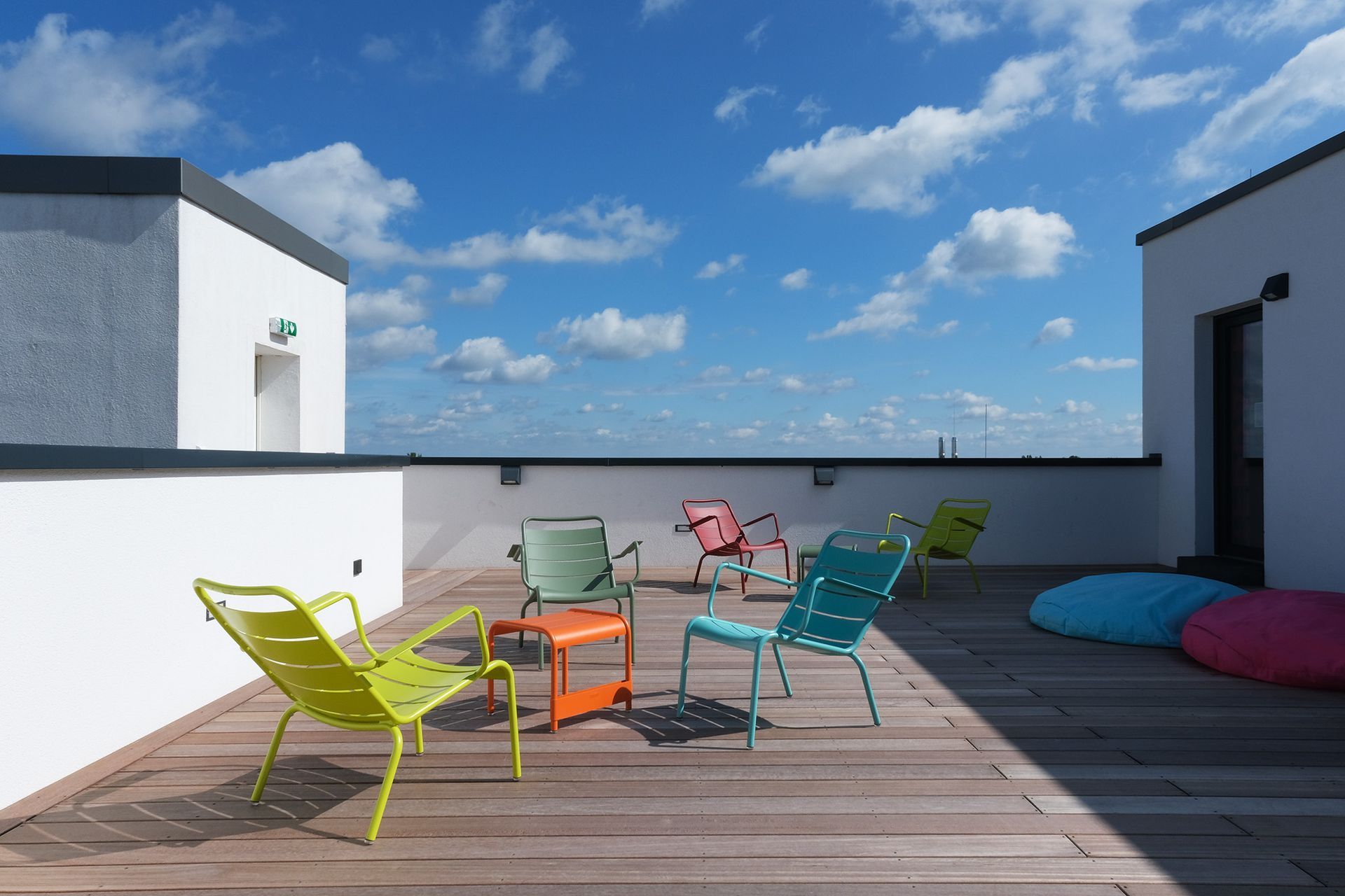 Dachterrasse mit bunten Stühlen und Sitzsäcken vor einem strahlend blauen Himmel mit Wolken.