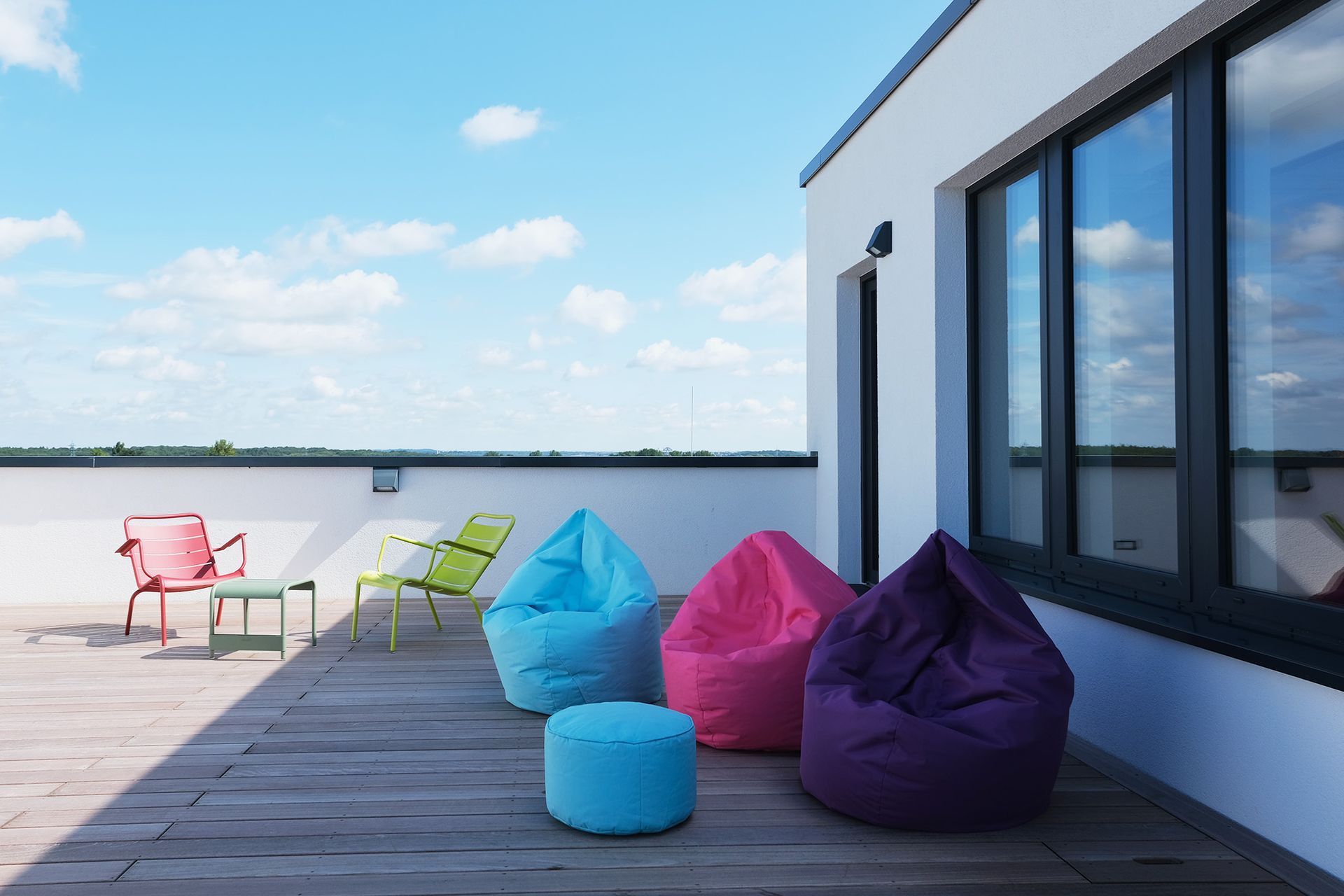 Lounge auf dem Dach mit bunten Sitzsäcken und Metallstühlen vor blauem Himmel.