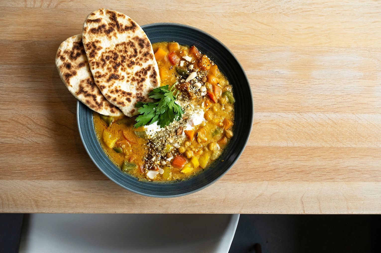 Eine Schüssel Linsencurry mit Naan-Brot auf einem Holztisch