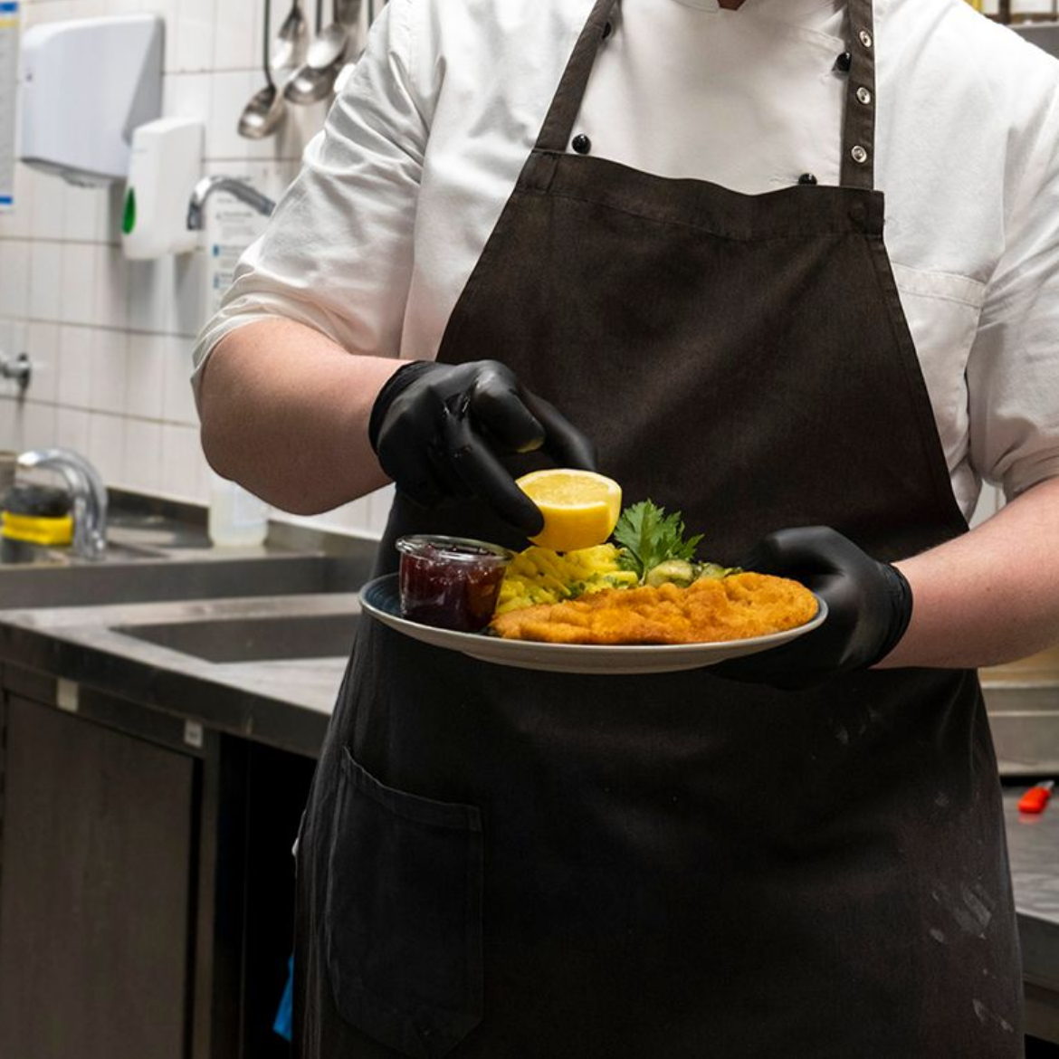 Ein Koch mit schwarzen Handschuhen richtet in einer Küche ein Schnitzel an.