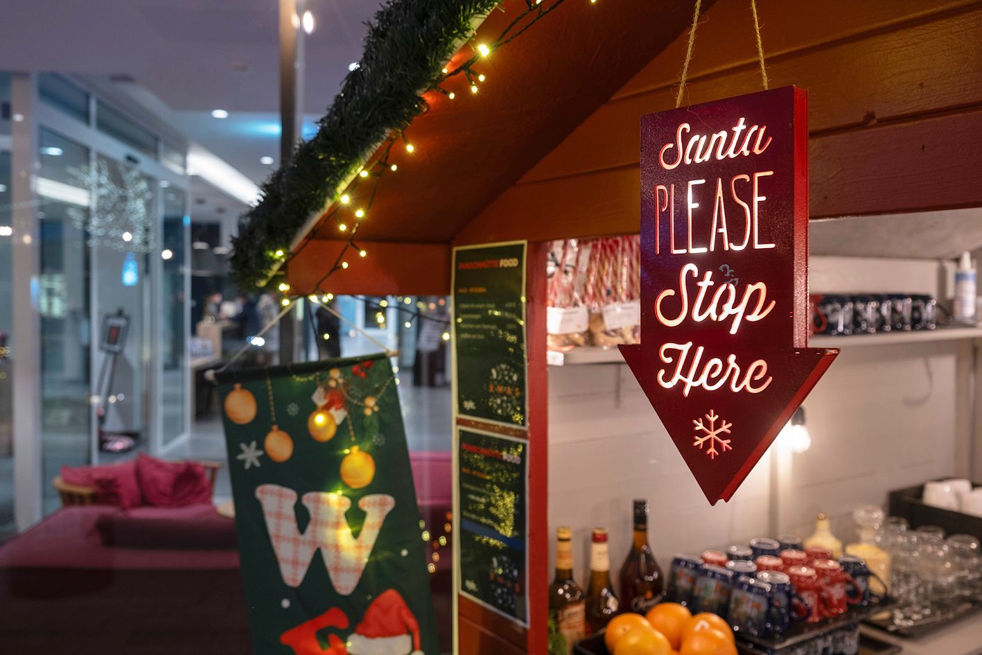 Weihnachtsgeschenkfassade mit einem roten Schild „Santa Please Stop Here“ und festlicher Dekoration auf dem Ladentisch.