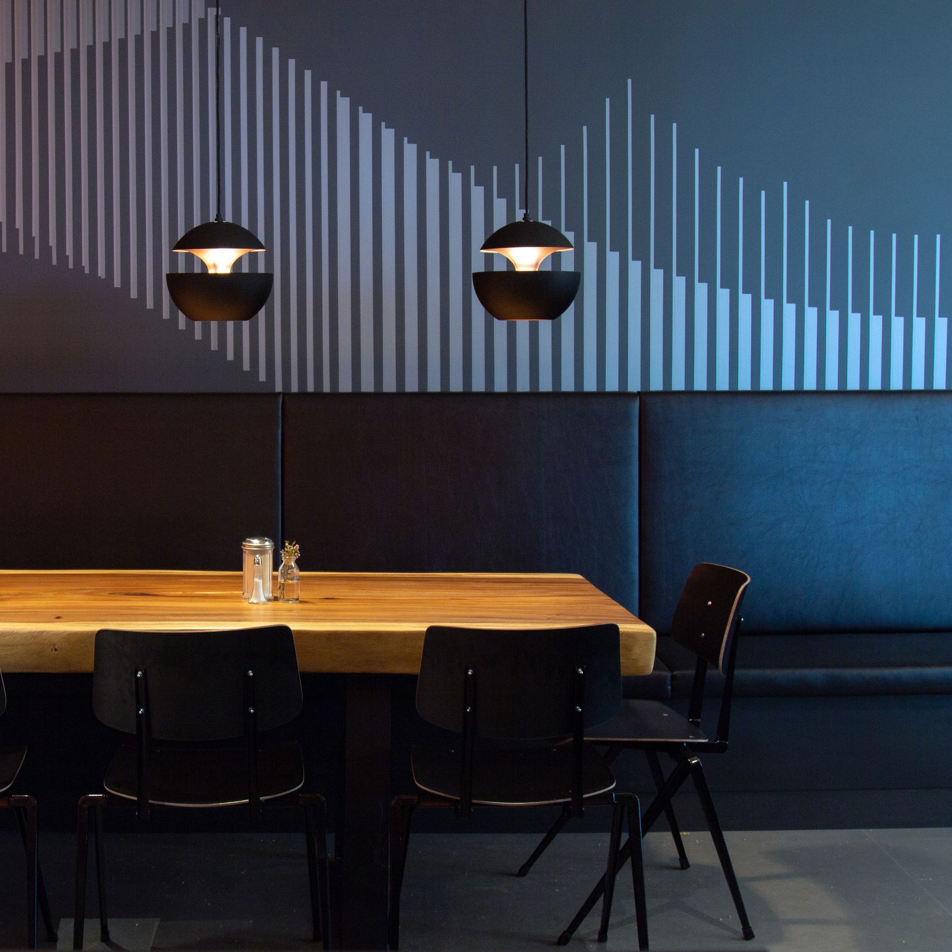 Ein Essbereich mit einem Holztisch, Stühlen und zwei Pendelleuchten. Die Wand hinter dem Tisch ist in Blau-Grau gehalten