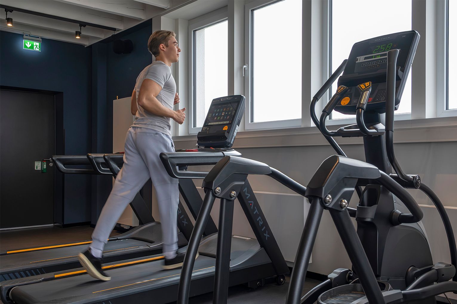 Ein Mann läuft auf einem Laufband in einem Fitnessstudio, in der Nähe eines Ellipsentrainers.