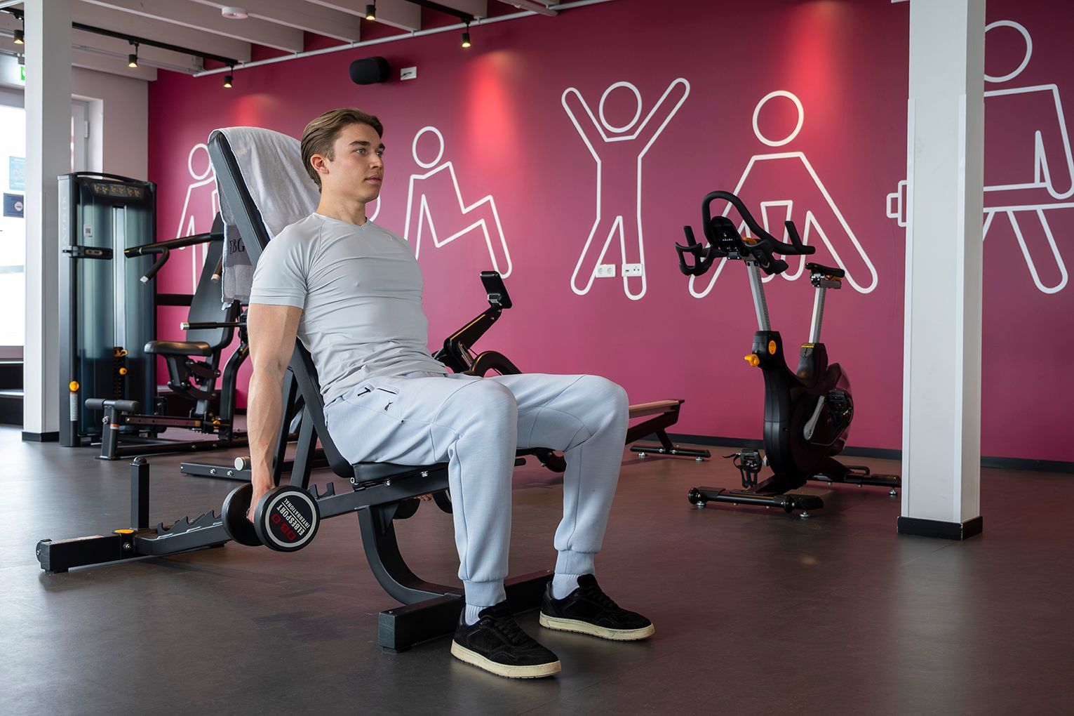 Person in weißem Hemd und schwarzen Leggings macht im Yoga auf einem rosa Sitzsack. Sie blickt weg und hat die Hände gefaltet
