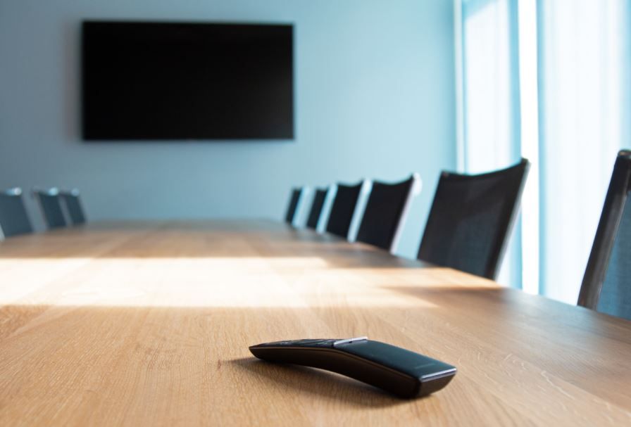 Eine Fernbedienung liegt auf einem Holztisch in einem Konferenzraum.