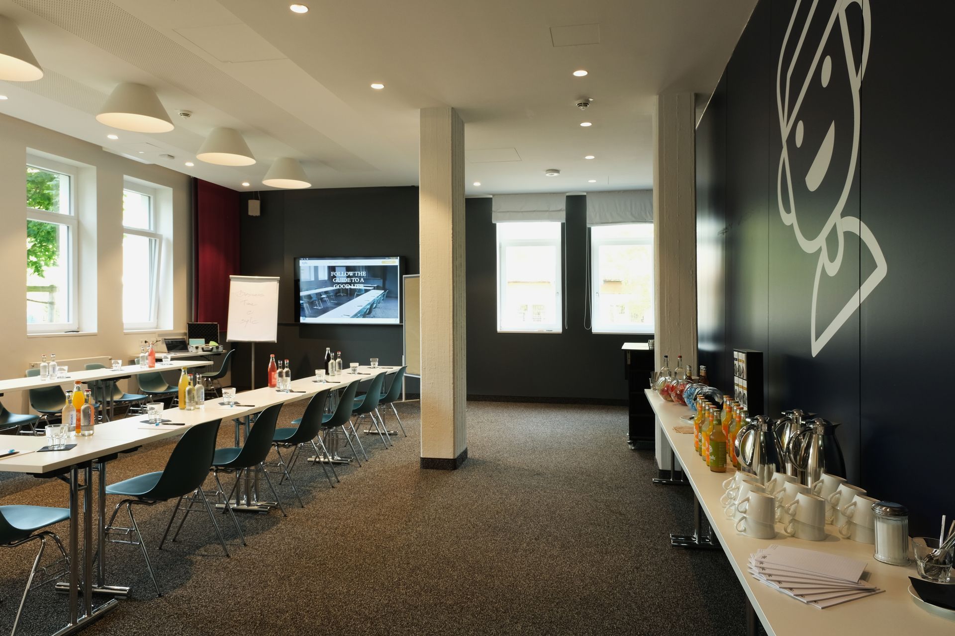 Konferenzraum mit für ein Meeting gedeckten Tischen, Getränken und Snacks. Verfügt über eine schwarze Wand.
