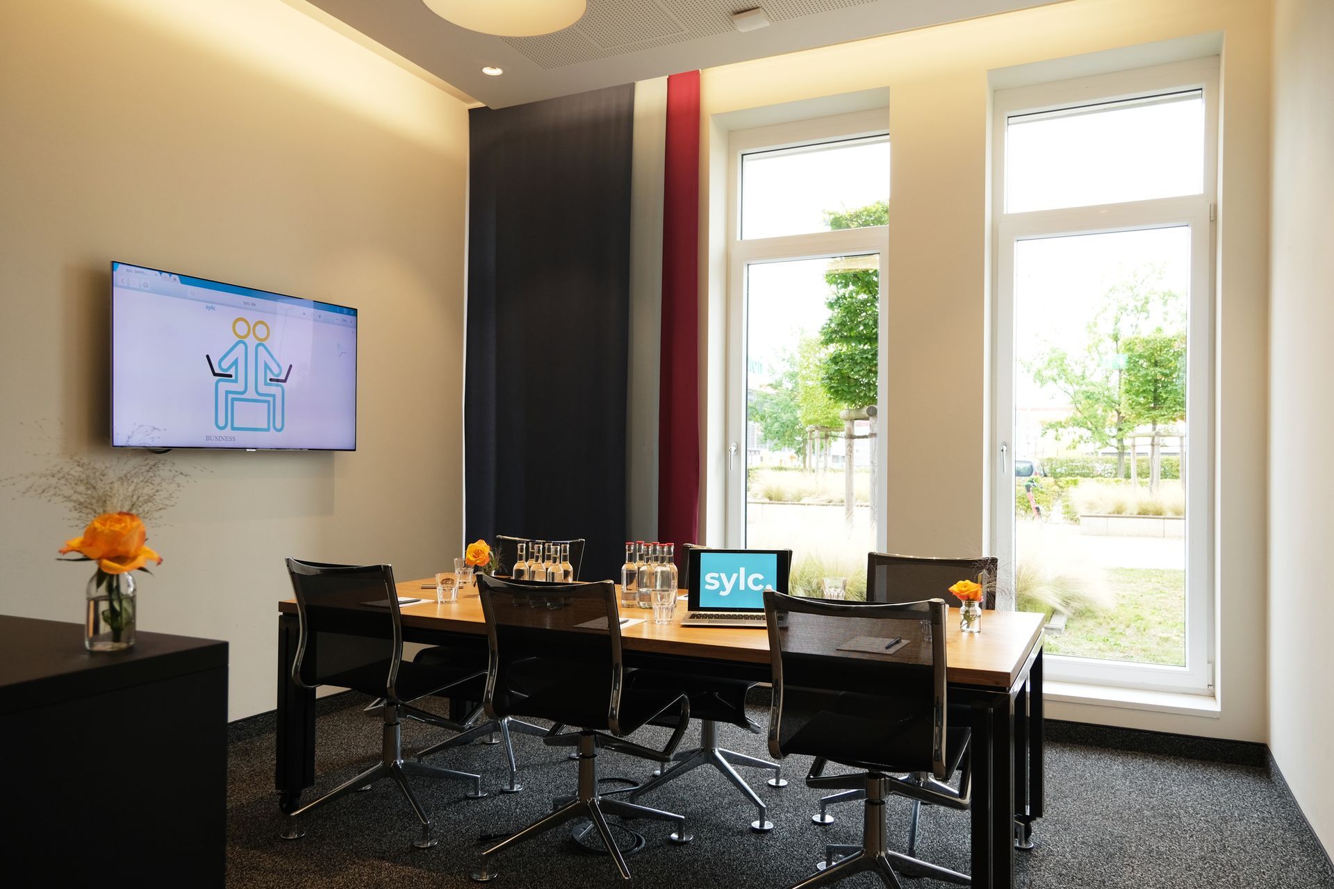 Ein Konferenzraum mit einem Tisch und Stühlen und einem Flachbildfernseher an der Wand.