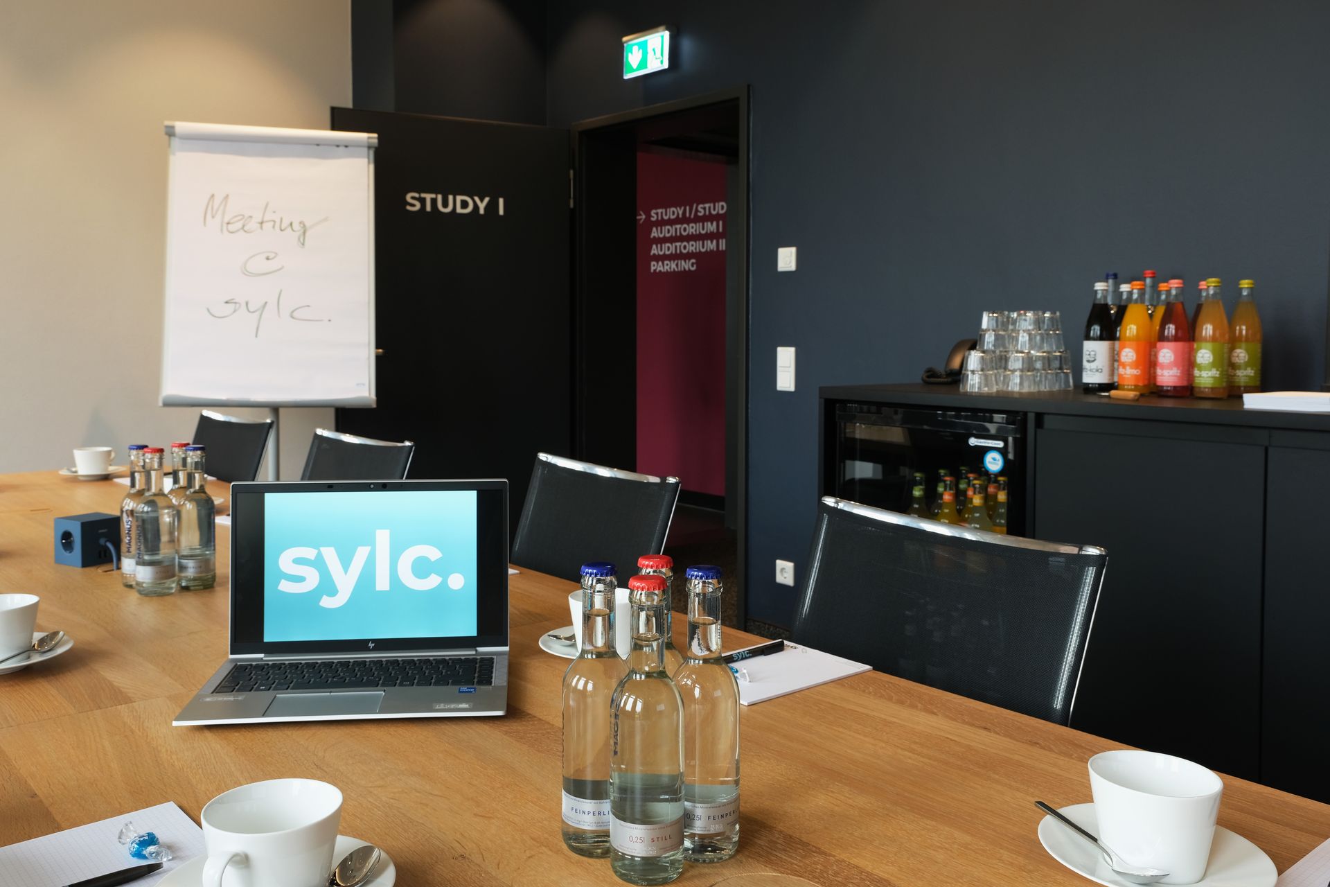 Ein Konferenzraum mit einem langen Holztisch, einem Laptop, Erfrischungen und einem Whiteboard mit Notizen.