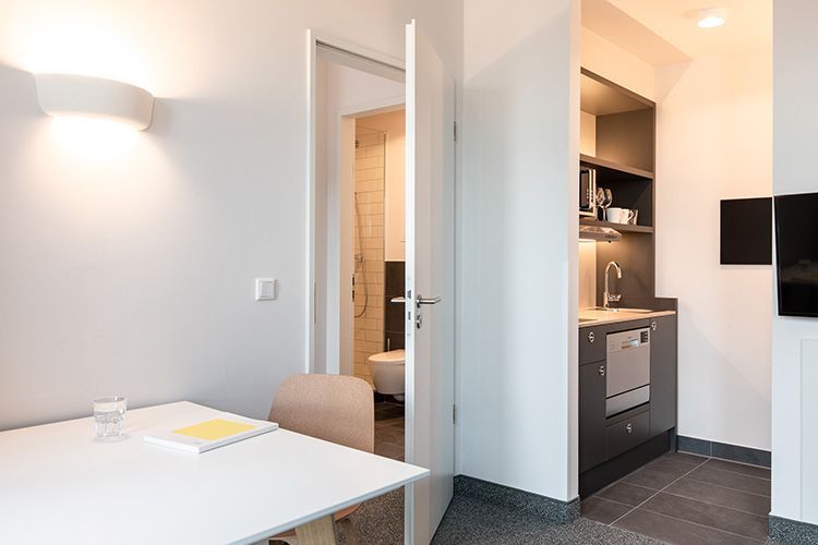 Kleine Wohnung mit Küchenzeile, Tisch und offener Tür zum Badezimmer. Der Raum ist minimalistisch und hell.