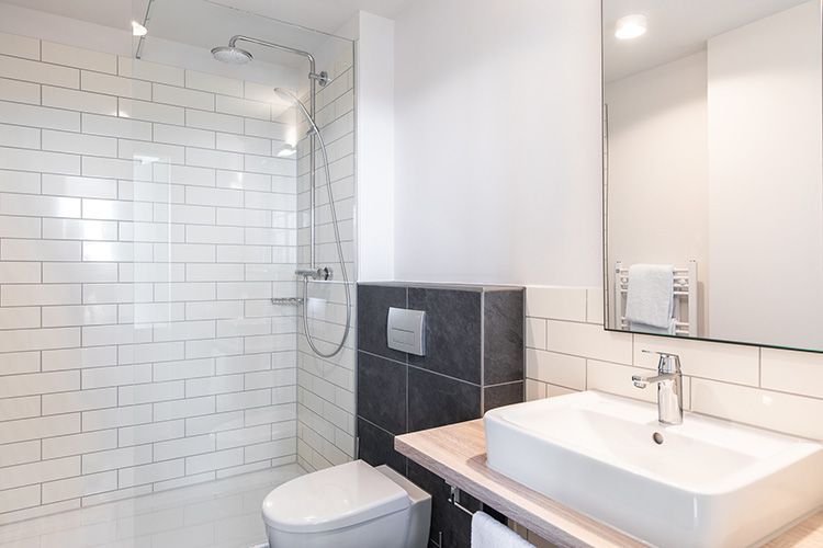 Modernes Badezimmer mit Dusche mit weißen U-Bahn-Fliesen, einem weißen quadratischen Waschbecken und einer Toilette.