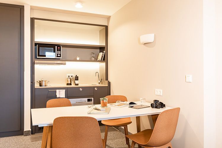 Eine Küche mit Tisch und Stühlen. Sie verfügt über eine Mikrowelle, eine Spüle und einen Schrank. Beige Wände und vier Stühle