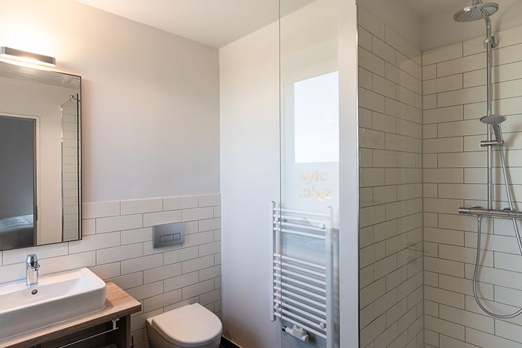 Modernes Badezimmer mit weißen U-Bahn-Fliesen, einer Glasdusche, Toilette, Waschbecken und Spiegel.