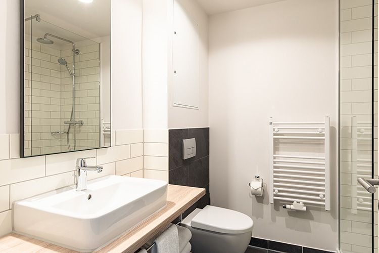 Modernes Badezimmer mit rechteckigem Waschbecken, Toilette, Dusche und Handtuchwärmer; Farbschema in Weiß und Grau.