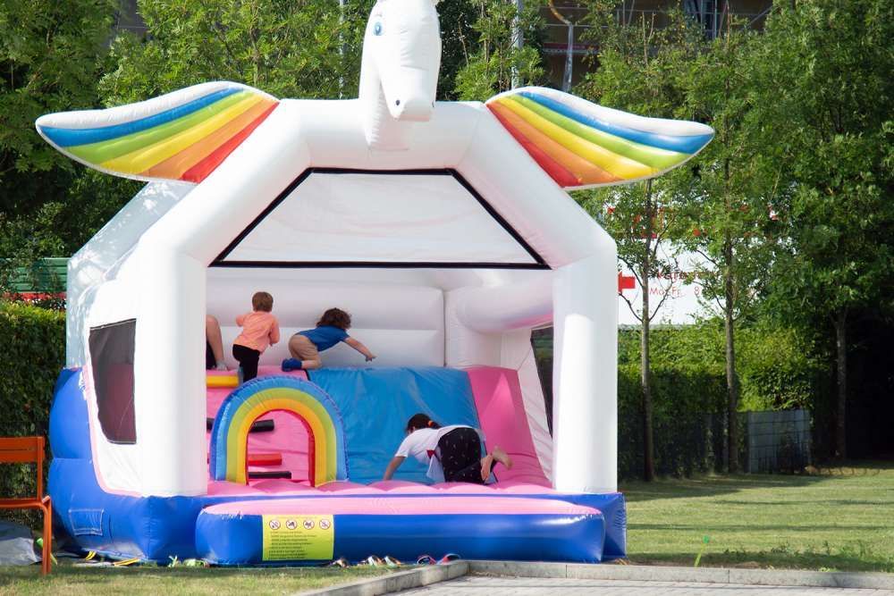 Kinder spielen im Freien in einer bunten, aufblasbaren Einhorn-Hüpfburg.