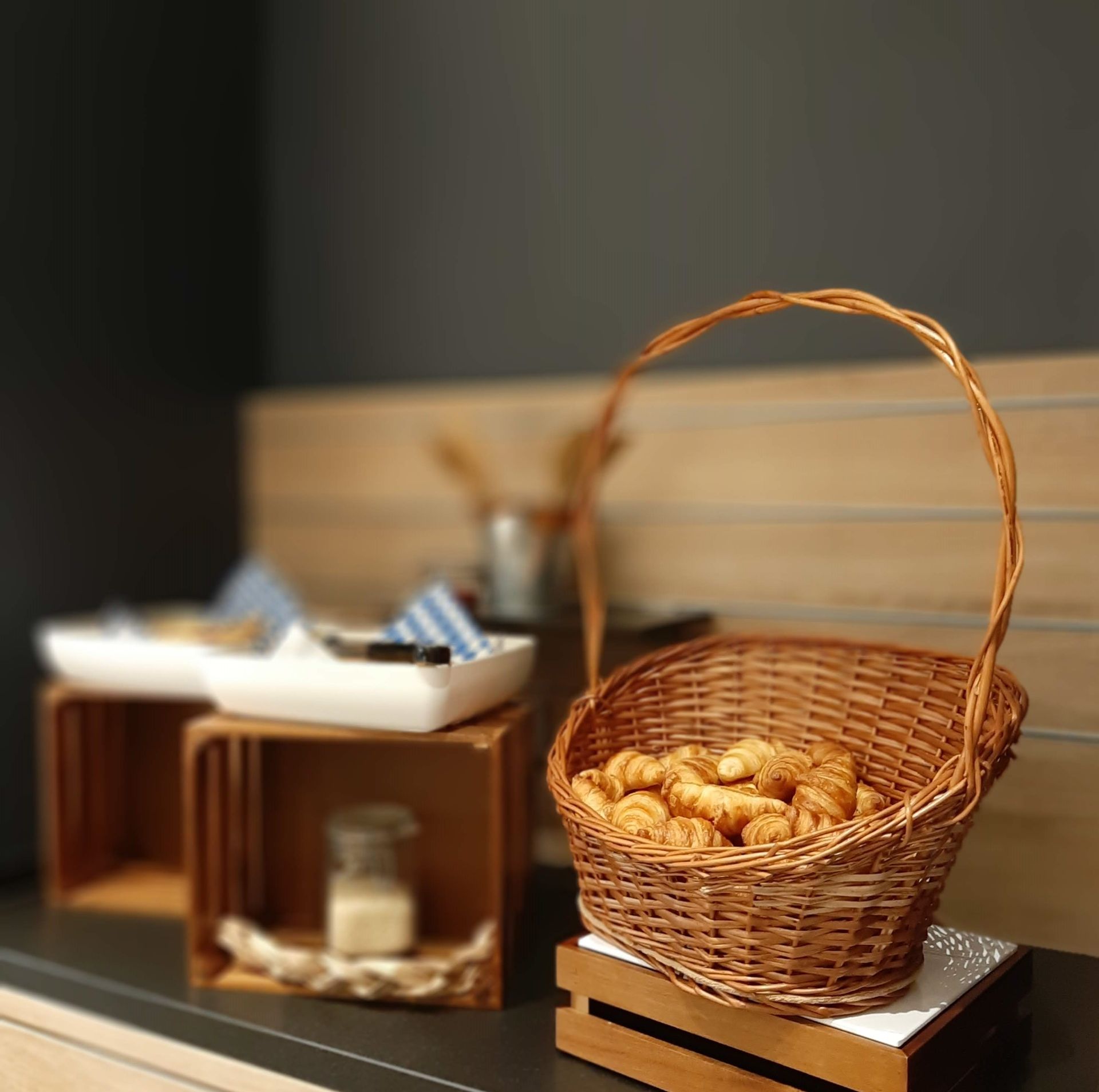 Ein Weidenkorb mit Croissants. Im Hintergrund sind weitere Backwaren, Behälter und eine dekorative Auslage zu sehen.