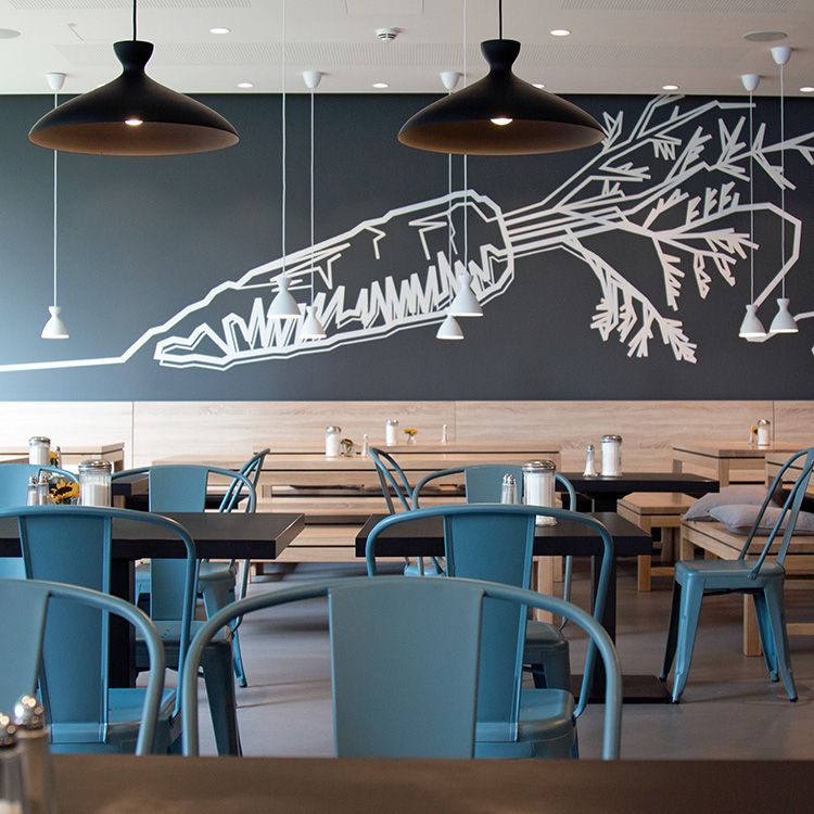 Stühle und Tische füllen ein modernes Restaurant mit dunkelgrauer Wand mit großer Wandillustration und Hängelampen.