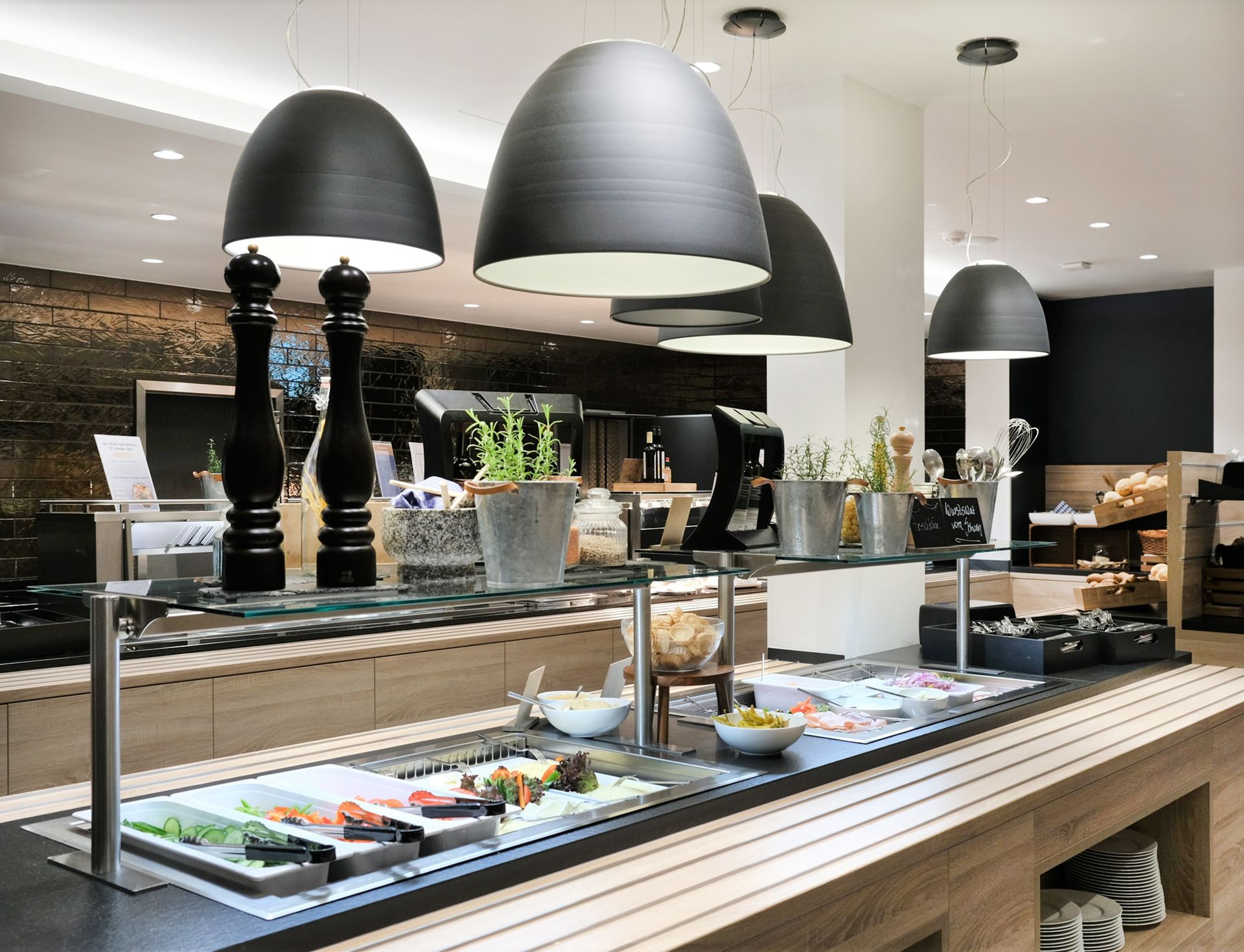 Buffet-Essbereich mit langer Theke, verschiedenen Gerichten und hängenden schwarzen Pendelleuchten.