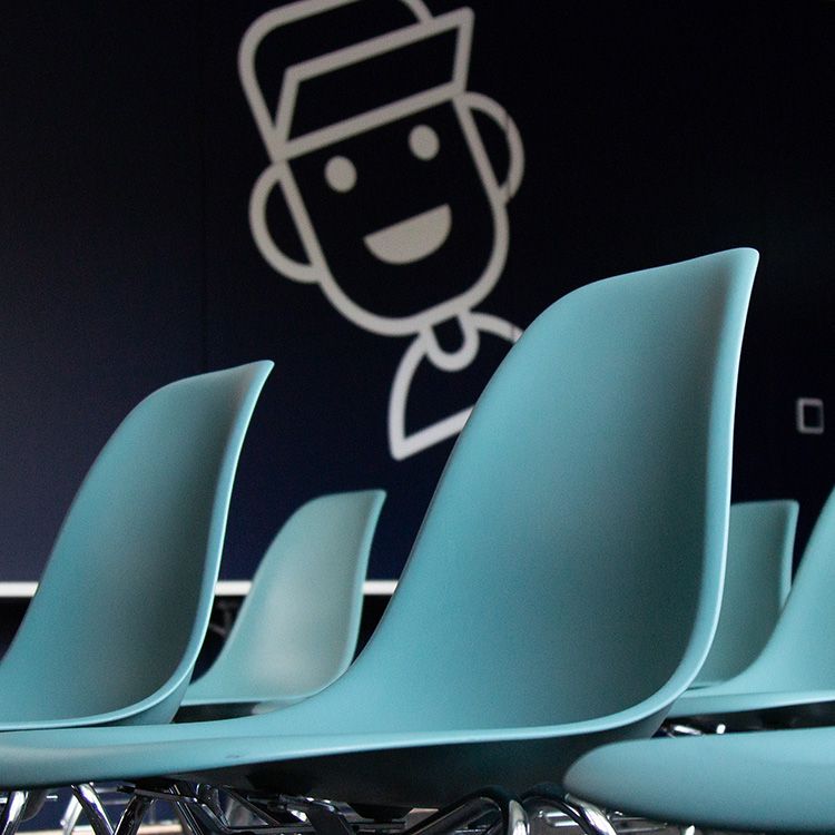 Teal plastic chairs in a row with a cartoon person smiling on the wall in the background.