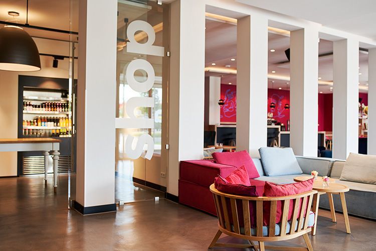 sylc. Apartmenthotel | Lobby | Almost Everything Shop | Library Bar Hotellobby mit Couch, Sessel und Tisch. Zu sehen sind zudem ein Shop und eine Hotelbar
