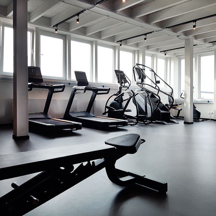 Ein Fitnessstudio mit Laufbändern und Steppern und einer Bank
