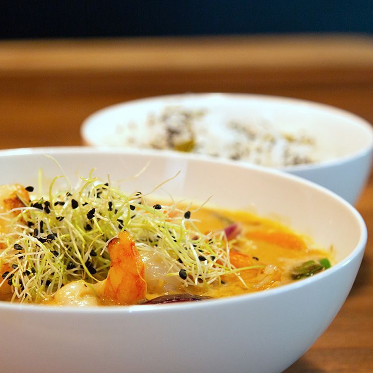 Eine Schüssel Suppe mit Garnelen und Sprossen neben einer Schüssel Reis auf einem Tisch.