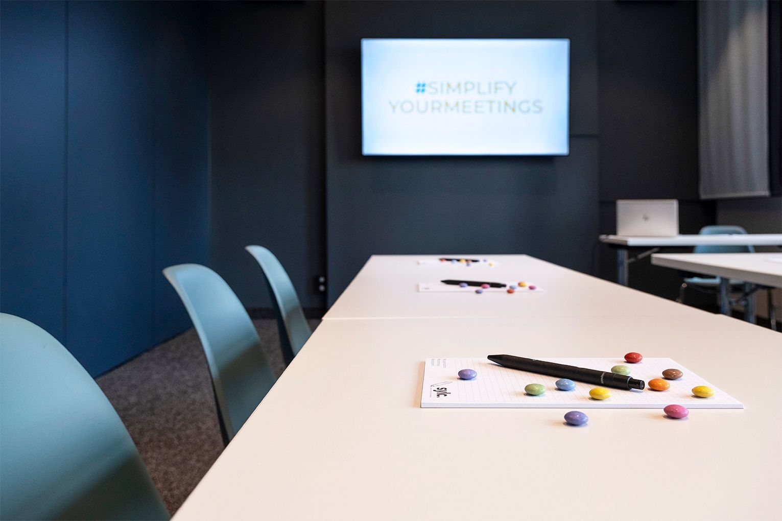 Meetingraum Study III mit langem Tisch, Stühlen und einer Wandleinwand, auf der eine Präsentation gezeigt wird