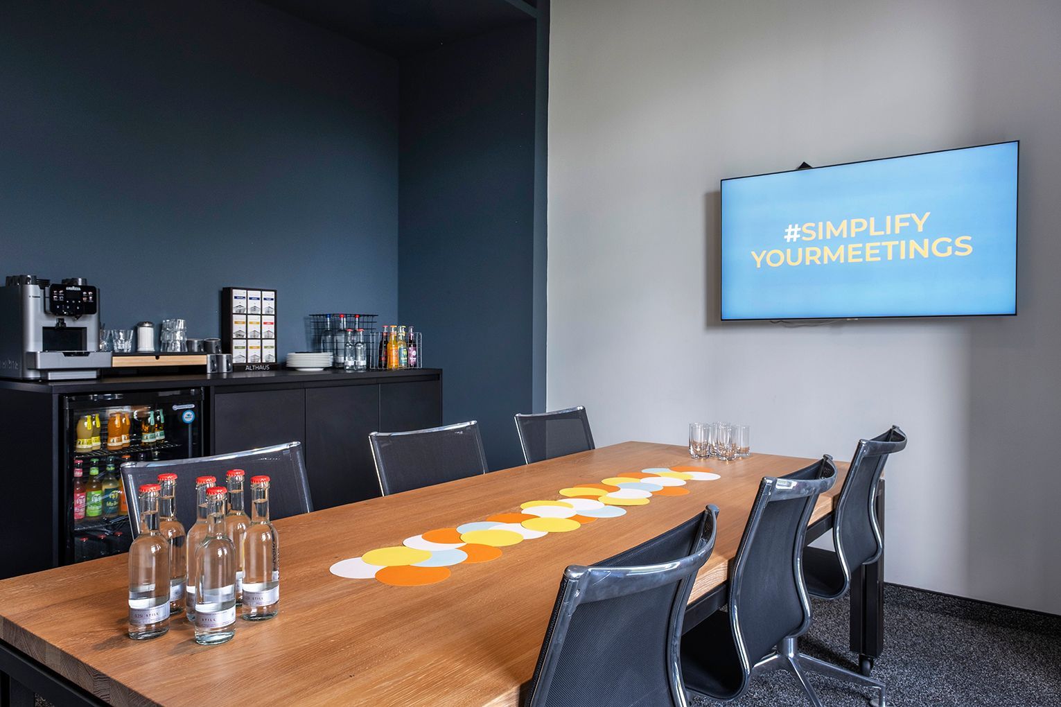Study II Meetingraum mit Holztisch, Stühlen, Regalen und an der Wand montiertem Bildschirm