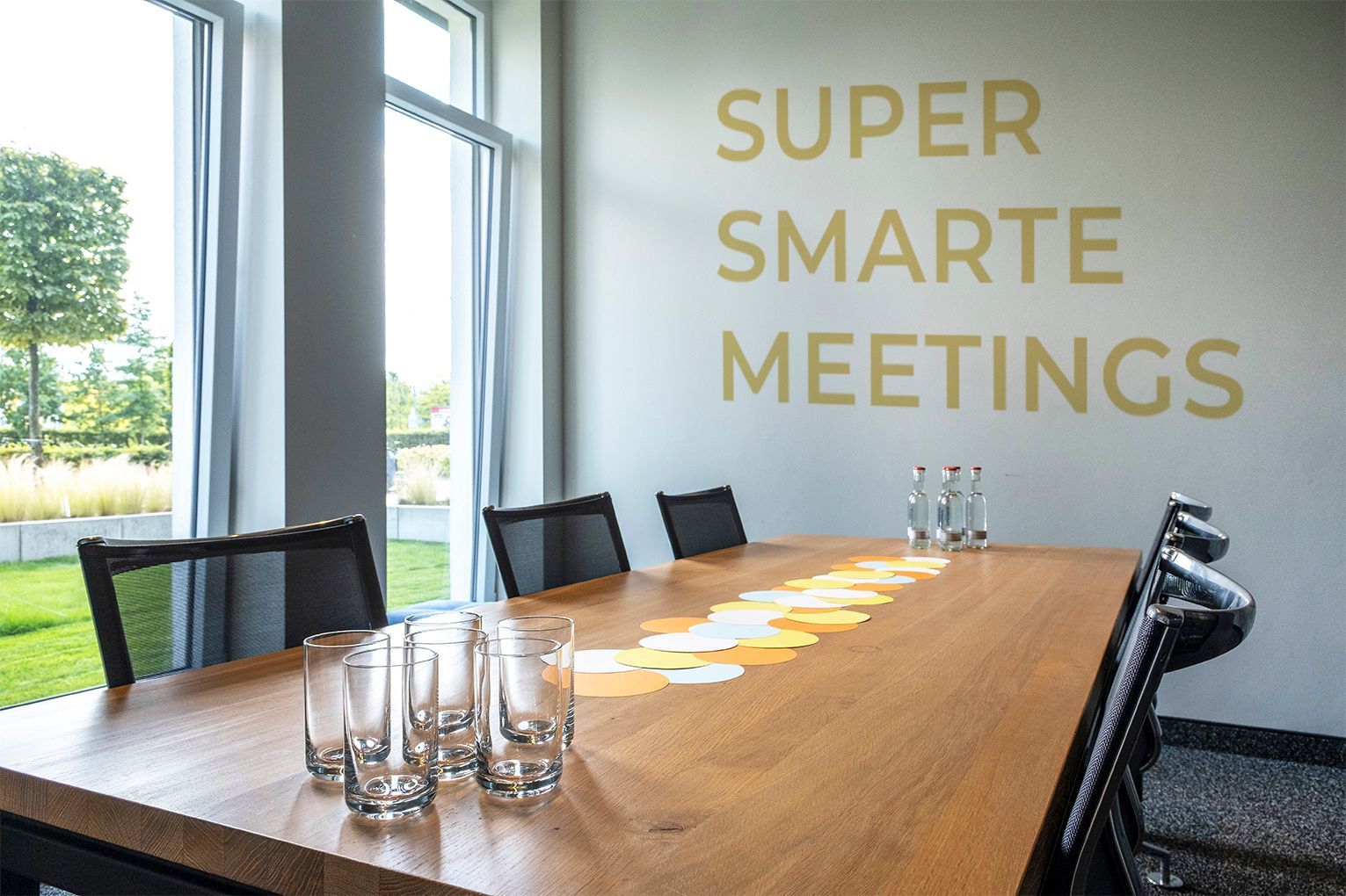 Study II Meetingraum mit langem Holztisch, Stühlen, Gläsern und dem Schriftzug „SUPER SMARTE MEETINGS“ an der Wand.