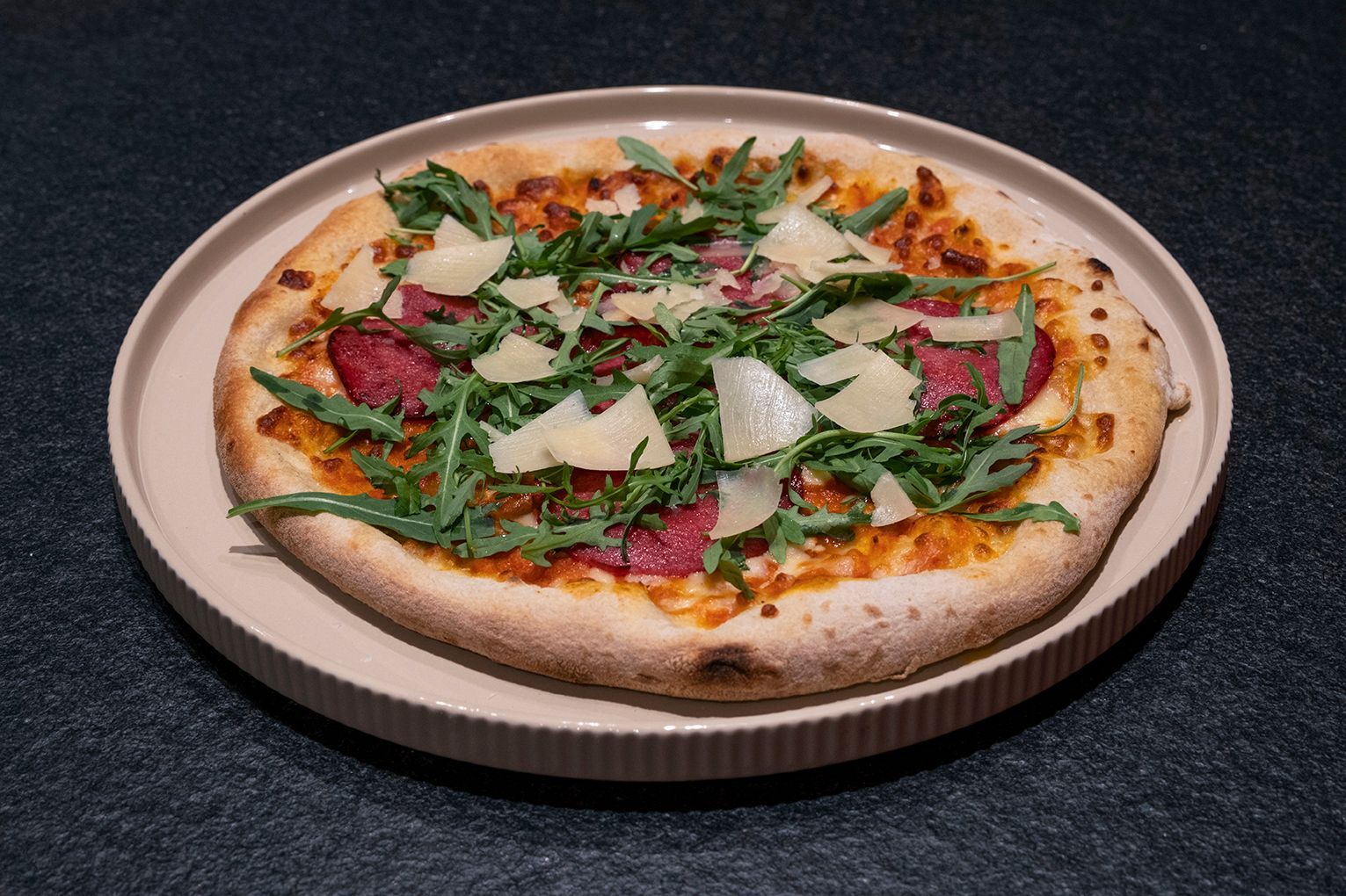 Gourmet-Pizza mit Rucola, Wurstwaren und gehobeltem Parmesan auf einem Teller