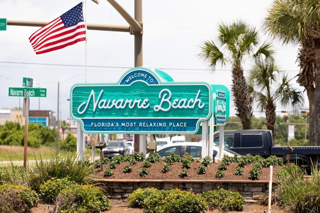 Sign for Navarre Beach, Florida, with U.S. flag. Green sign reads 