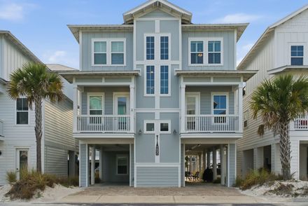 Beachfront house with gray siding, white balconies, and palm trees on either side