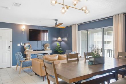 Living and dining area at Sunset Harbor Villas 322 with a tan leather sofa, long wood dining table and sliding glass doors to the balcony