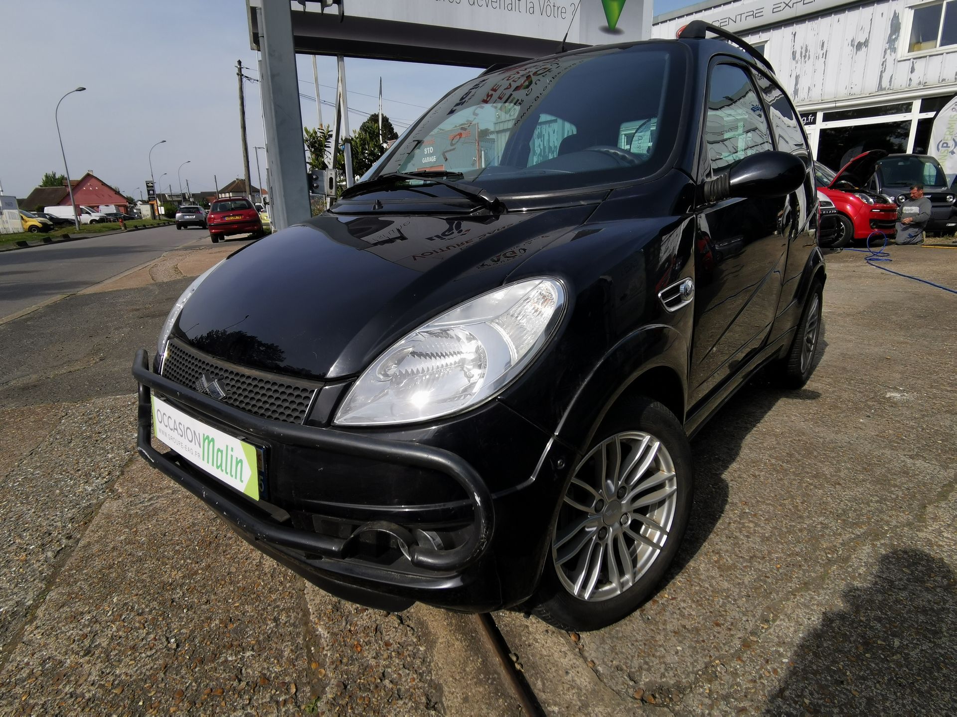 Une microvoiture noire deux portes est garée sur le trottoir, au bord d'une rue.