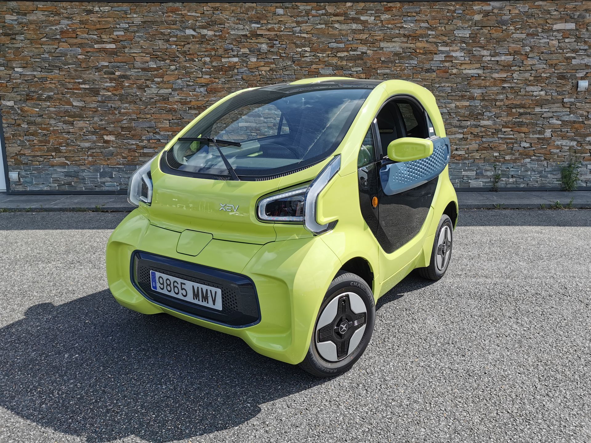 Voiture électrique jaune vif garée sur l'asphalte devant un mur de briques.
