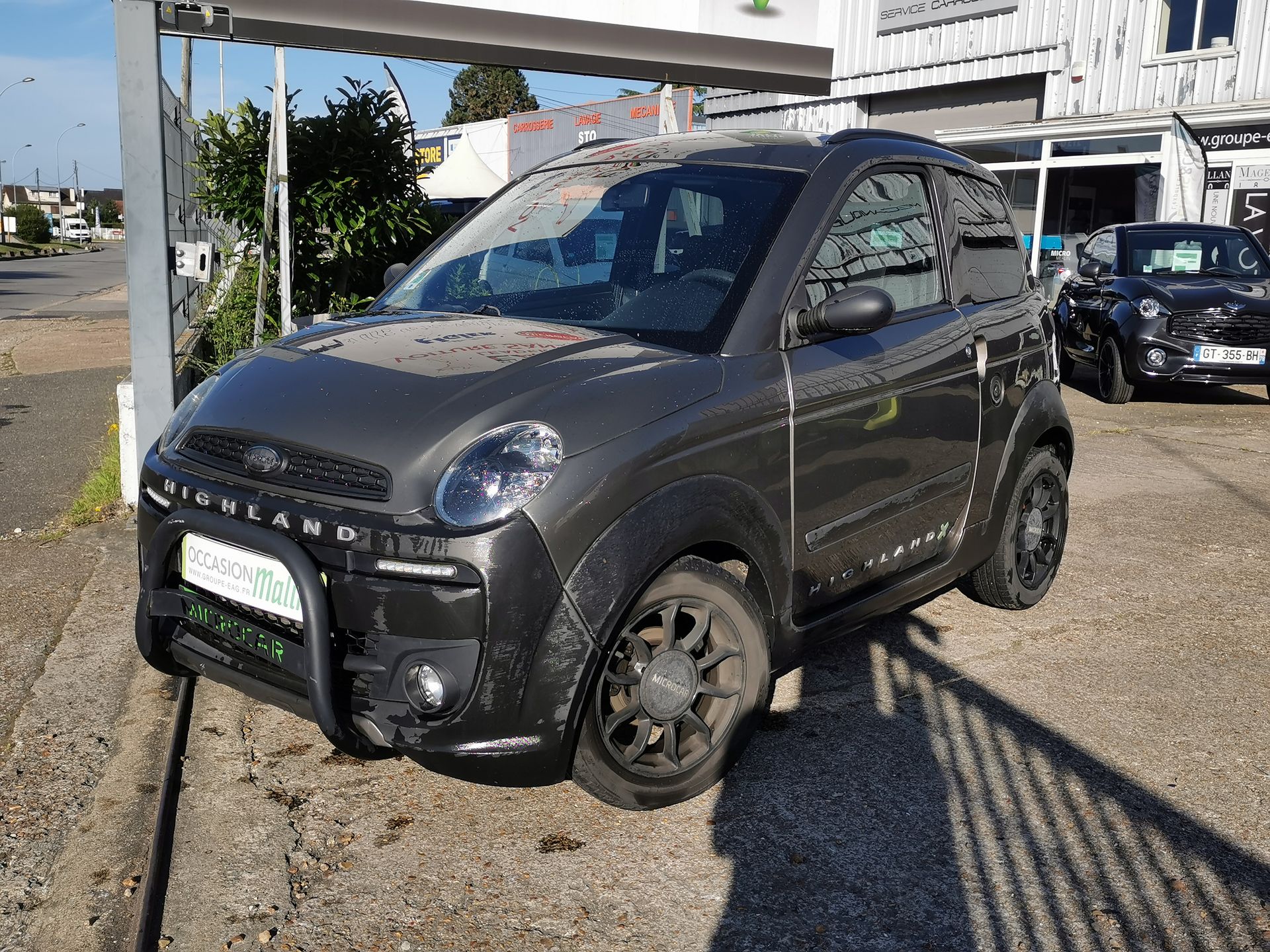 Une voiture sans permis grise garée sur le trottoir devant une concession automobile.