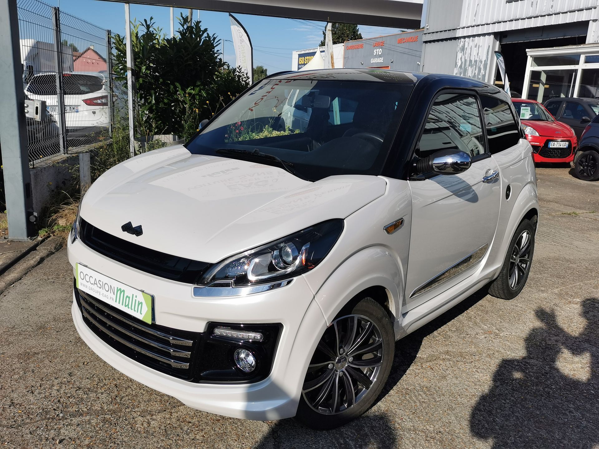 Voiture blanche deux portes à toit noir garée devant un bâtiment.