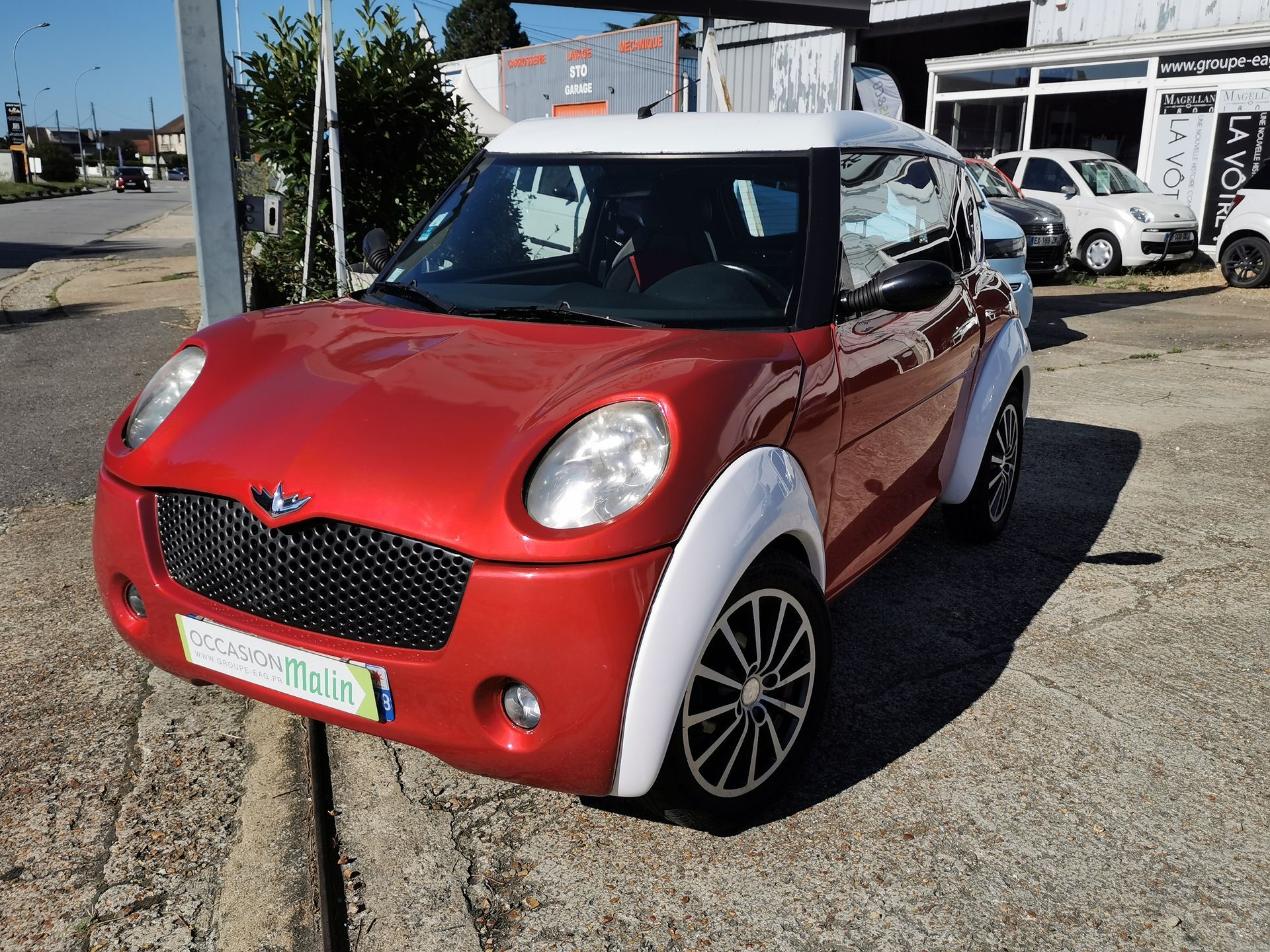 Voiture deux portes rouge et blanche avec calandre noire, garée dans la rue.