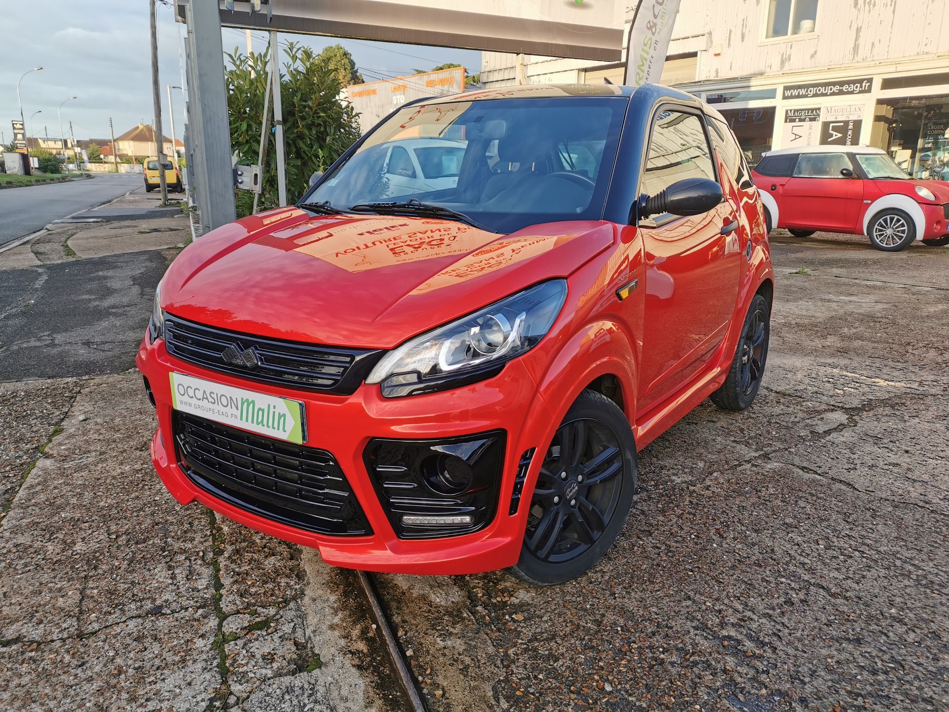 Micro-voiture rouge et noire garée sur un trottoir.