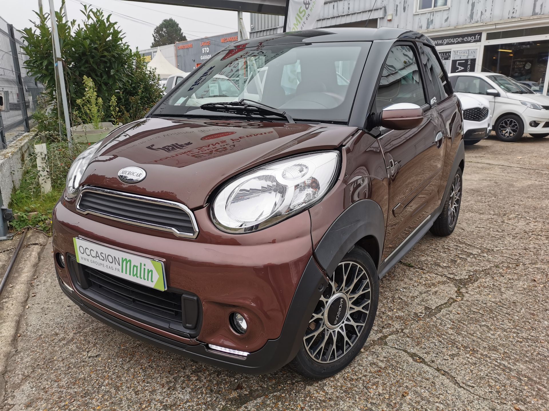 Une microvoiture marron avec des touches de noir est garée sur un parking goudronné.