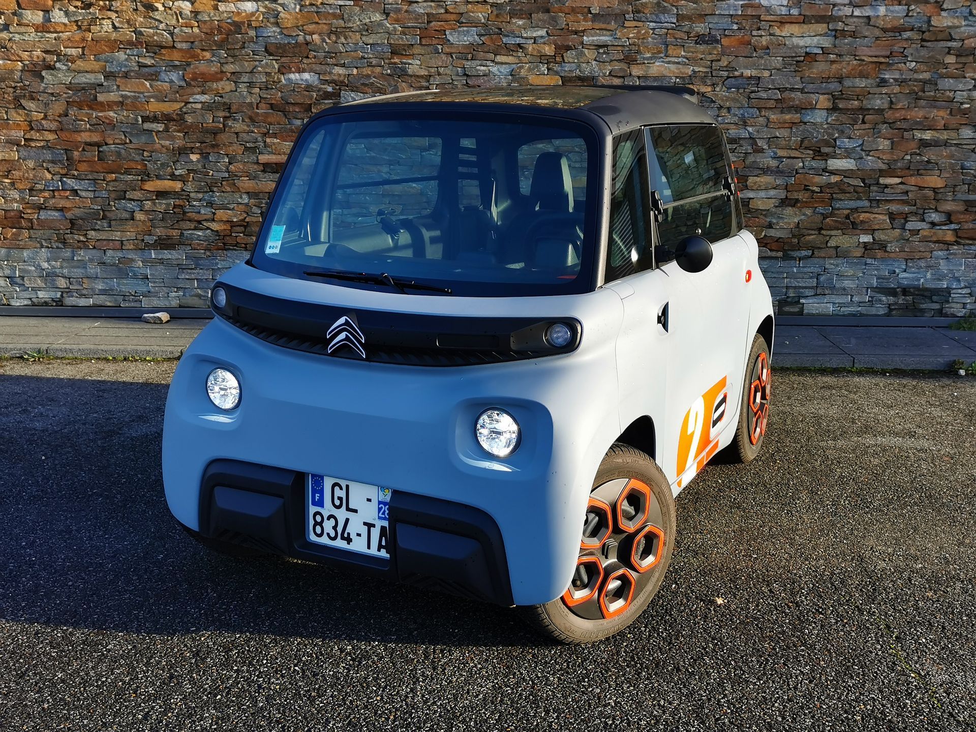 Citroën Ami électrique bleue garée devant un mur en pierre, jantes orange.