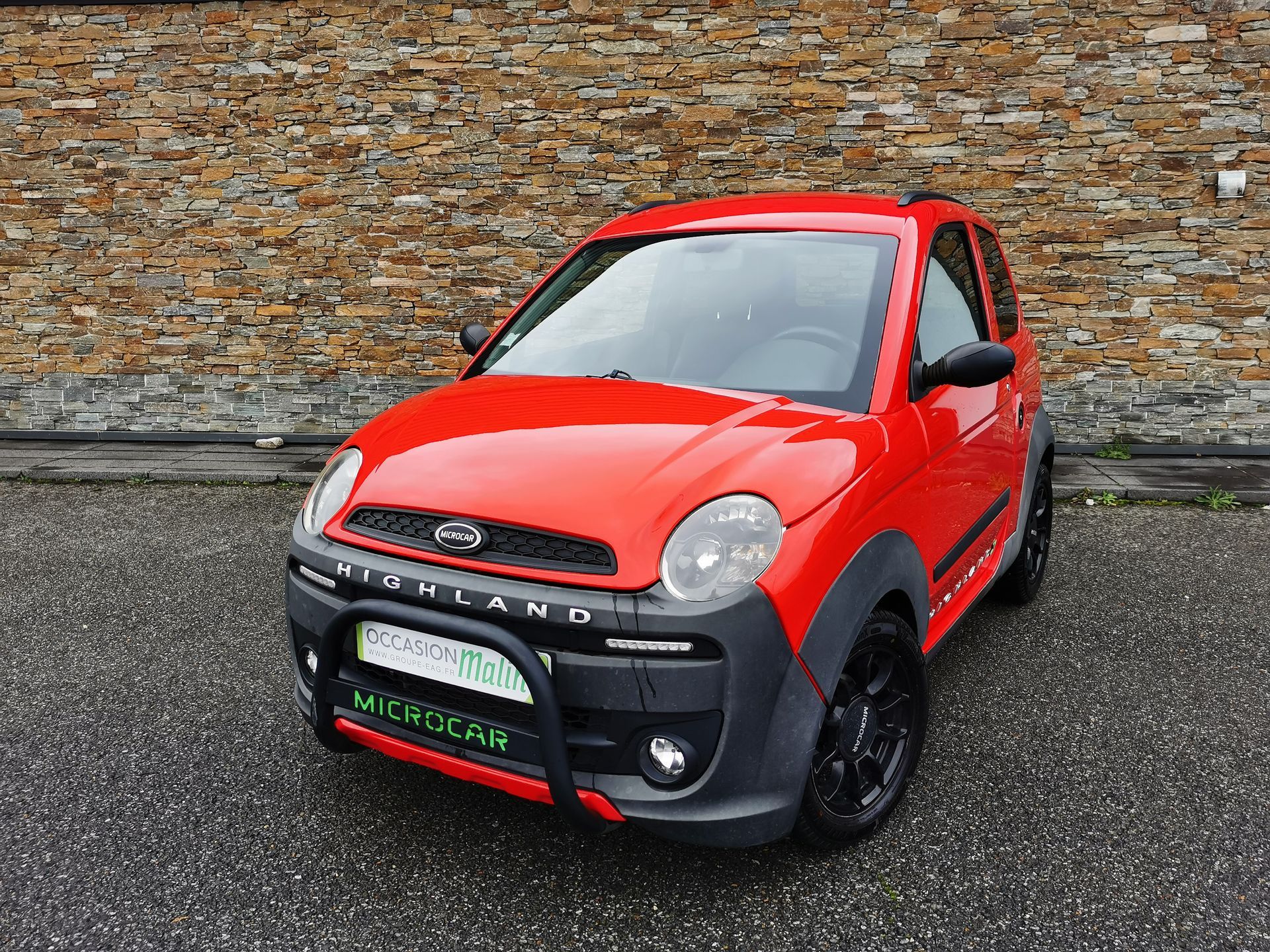 Voiture rouge Aixam Mega City avec des accents noirs garée devant un mur de briques.