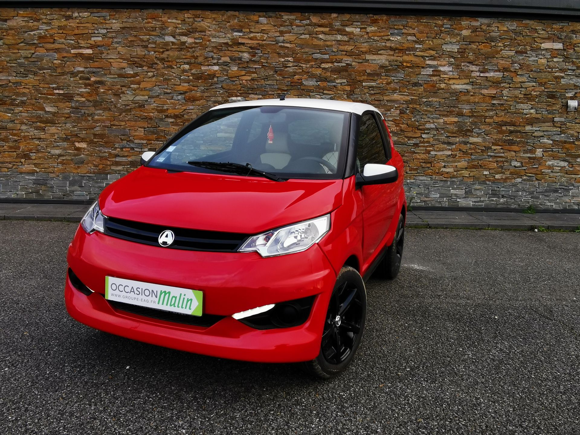 Voiture compacte rouge et blanche garée devant un mur de briques. Jantes noires.