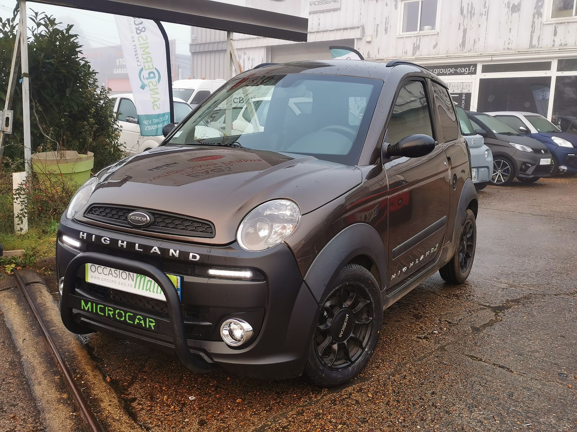 Microcar Brown Highland garée devant un bâtiment.