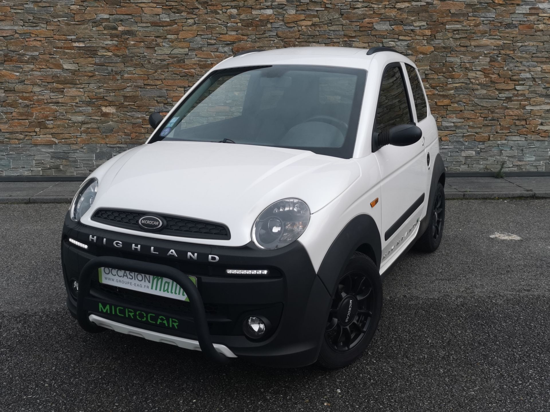 Voiture sans permis blanche Highland avec des garnitures noires garée devant un mur en pierre.