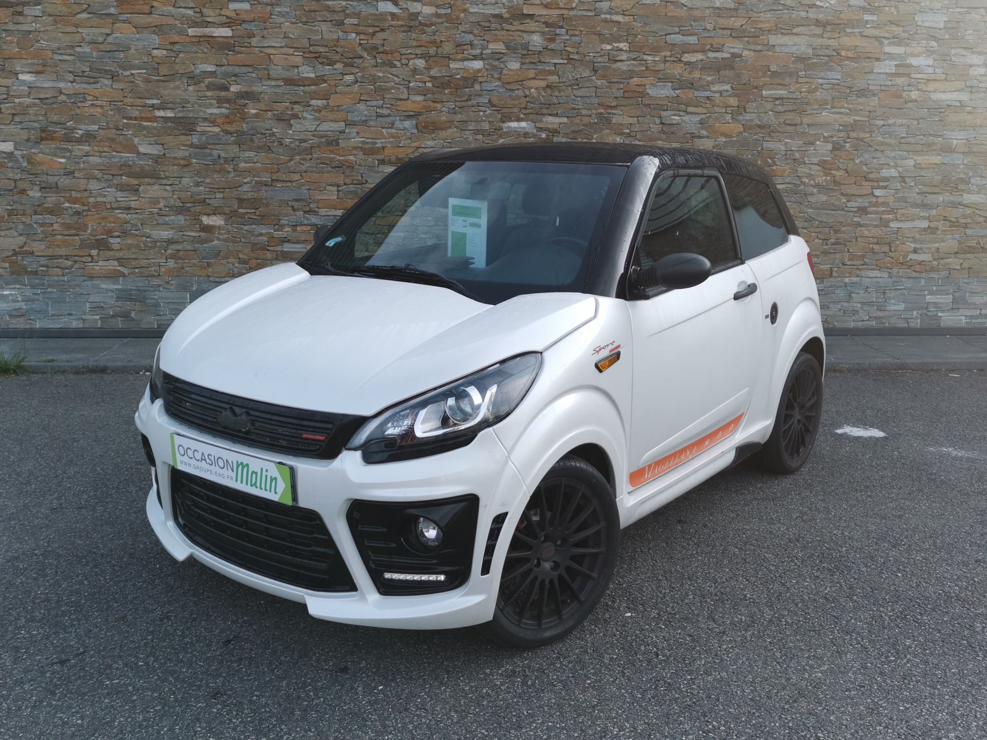 Voiture compacte blanche et noire garée devant un mur de briques.