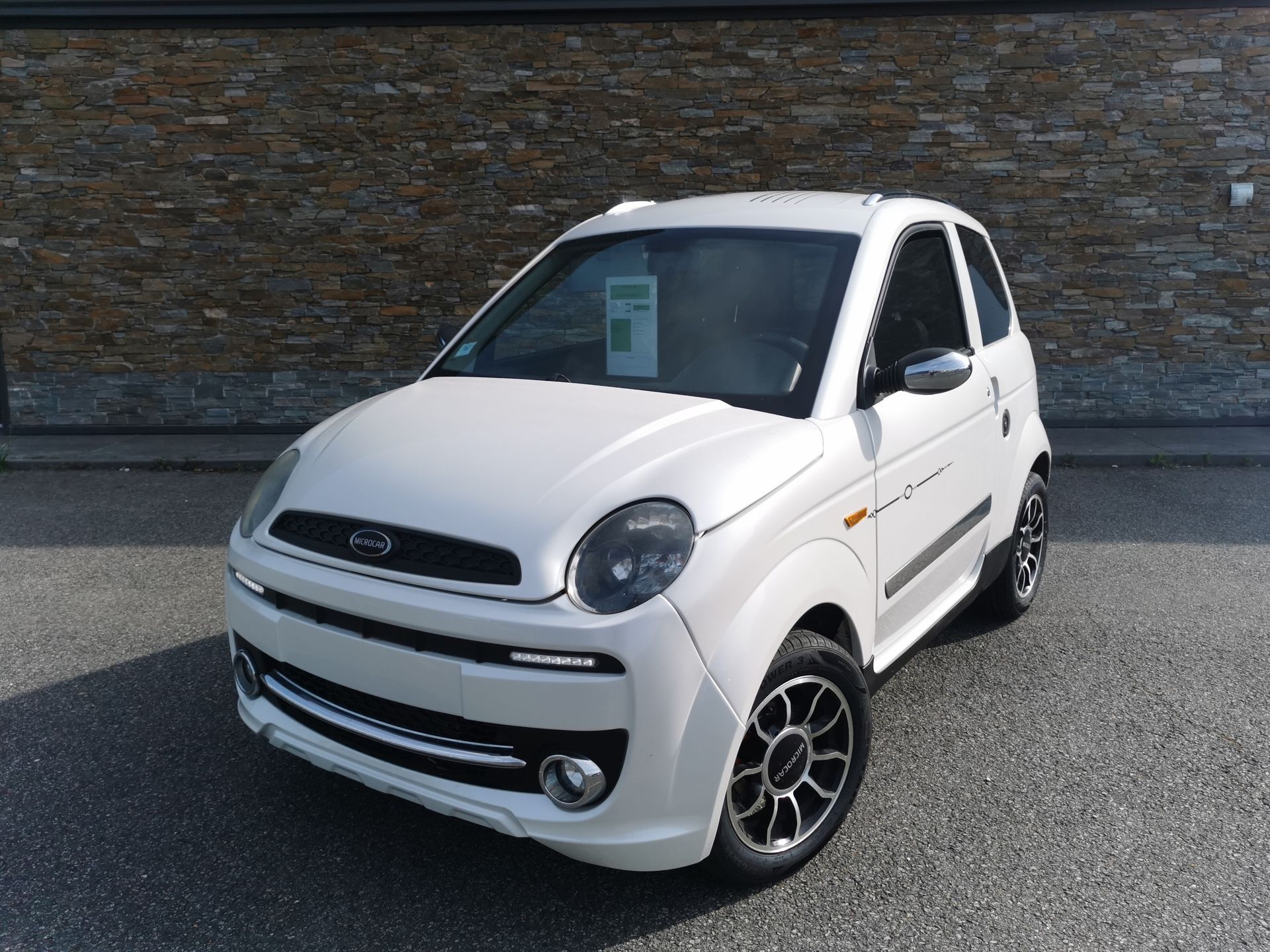 Voiture compacte blanche garée devant un bâtiment en briques.