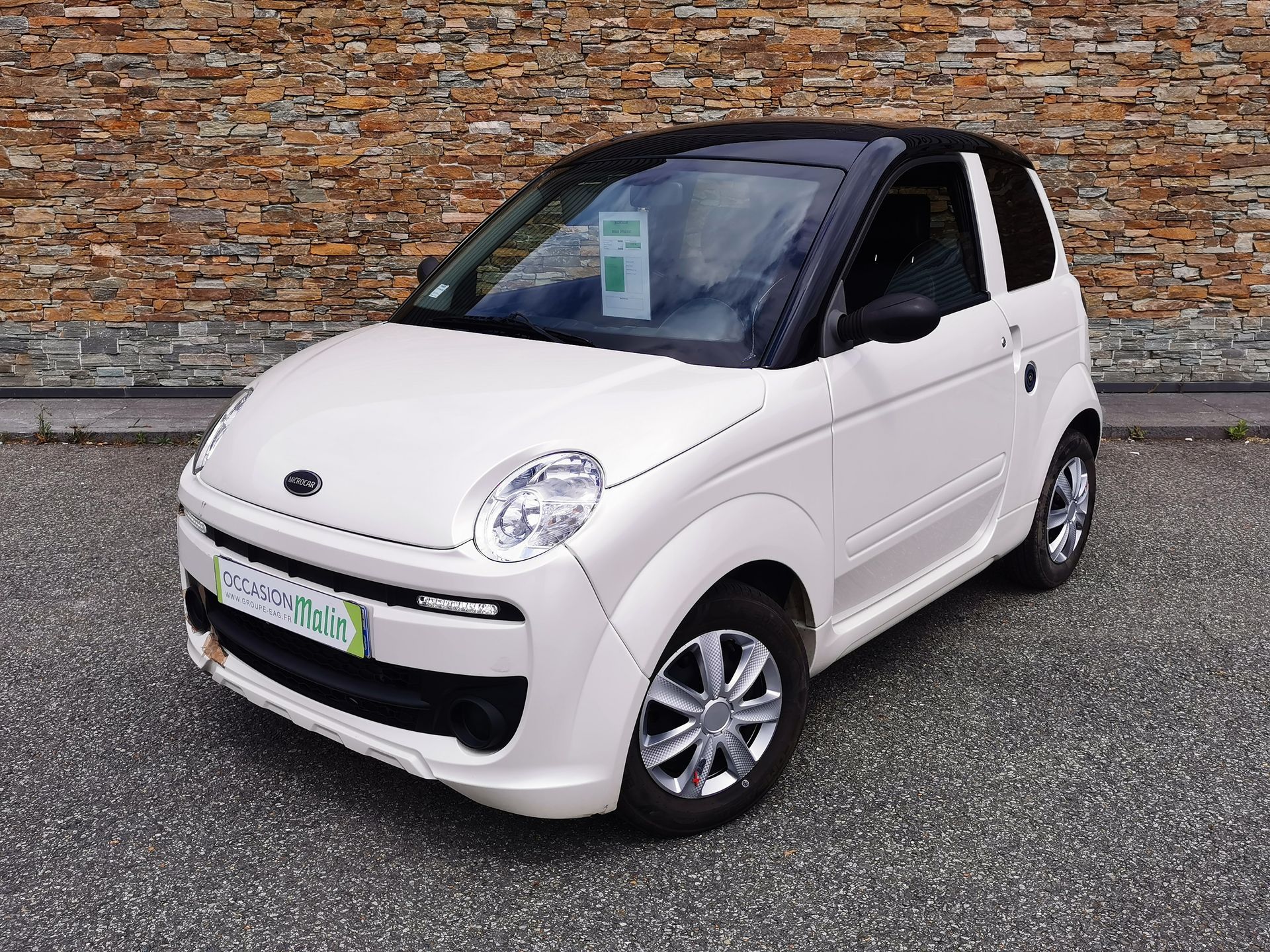 Microvoiture blanche et noire garée sur l'asphalte.