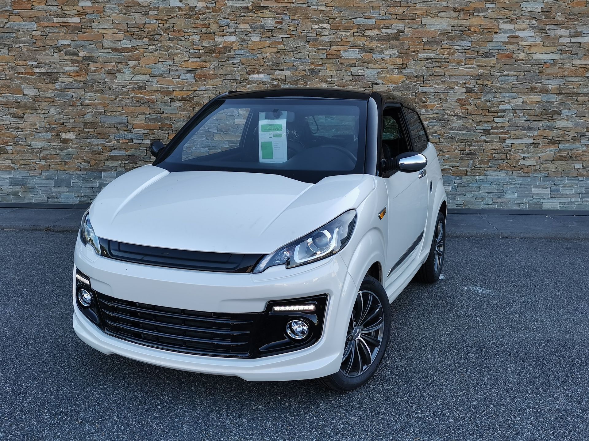 Voiture compacte blanche et noire garée devant un mur en pierre.