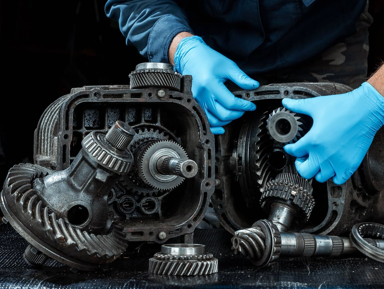 Un hombre que lleva guantes azules está trabajando en una caja de cambios.